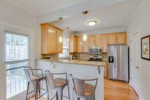 A kitchen with wooden cabinets, stainless steel appliances, a bar area with chairs, and a balcony with a railing. - Two Modern Home Retreat Near Downtown! Sleeps 18! (Nashville)
