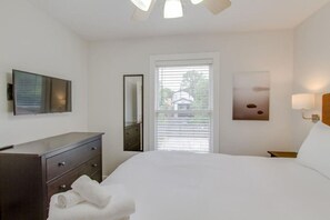Ein Hotelzimmer mit einem Bett, einem Schminktisch, einem Spiegel, einem Fenster mit Jalousien und einer Wandleuchte.