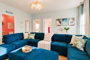 Ein Wohnzimmer mit einem blauen Ecksofa, einem kleinen Couchtisch und einer dekorativen Deckenleuchte.