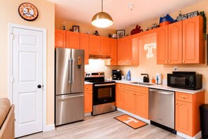 A compact kitchen with orange cabinetry, stainless steel appliances, and a white door. - Rocky Top + Boho Nashville Duo | Sleeps 12 (Nashville)