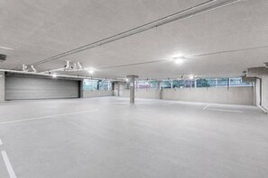 Garagem de estacionamento vazia, com pisos e paredes de concreto, iluminação no teto e porta fechada.