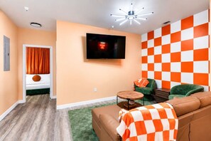 Ein Wohnzimmer mit Fernseher, einer Couch, einem Sessel und einer karierten Wand.