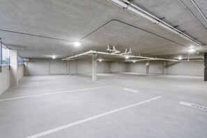 Garagem de estacionamento vazia, com piso e paredes de concreto, linhas de estacionamento brancas e iluminação superior.