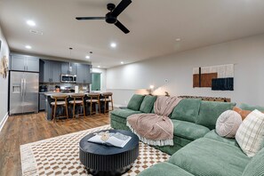 A modern living room with a green sofa, a coffee table, and a kitchen area with a refrigerator and bar stools. - Nashville Stay Near Downtown | 3BR on Fern Ave (Nashville)