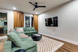 Uma sala de estar moderna com um sofá verde, uma mesa de centro preta e um tapete estampado.