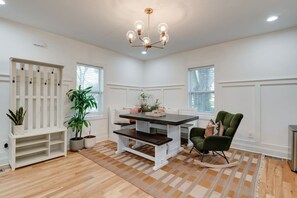 Een kamer met een eettafel, stoelen, een bankje, potplanten en een kroonluchter.