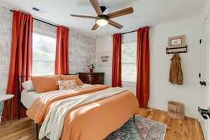 Een slaapkamer met een bed, een plafondventilator, een dressoir, een kapstok aan de muur en een raam met gordijnen.