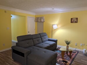 A living room with a dark grey sofa, a glass coffee table, a patterned rug, a floor lamp, and a door leading to another room. - 3-bedroom townhome in lovely Lithonia with cool AC (Lithonia)