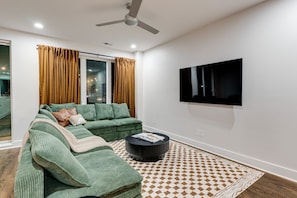 A modern living room with a sectional sofa, a flat-screen TV mounted on the wall, and a patterned rug on the floor. - Music City Luxury Walk Out Deck | Spacious 3BR Home (Nashville)