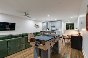 A modern living space with a ping pong table, green sofa, kitchen area, and a dining table with chairs. - Stylish Nashville Getaway • Cozy 3BR Near Downtown (Nashville)