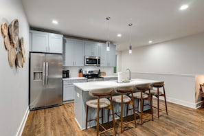 Una cocina moderna con una isla central, taburetes de bar, electrodomésticos de acero inoxidable e iluminación colgante.