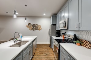 A modern kitchen with a central island, stainless steel appliances, and a decorative wall piece. - Stylish Nashville Getaway • Cozy 3BR Near Downtown (Nashville)