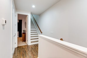 A hallway with a wooden floor, a white door, and a staircase with a wooden handrail. - Stylish Nashville Getaway • Cozy 3BR Near Downtown (Nashville)