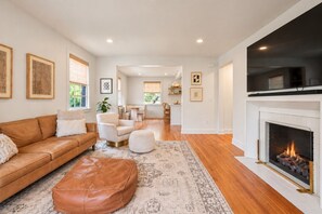 A spacious living room with a leather sofa, ottoman, and a fireplace. - Pet Friendly Home Near Vanderbilt & Centennial Park | 6-BR Home (Nashville)
