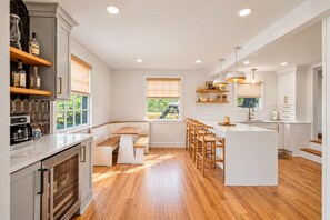 A modern kitchen with wooden flooring, white cabinetry, and a central island with bar stools. - Pet Friendly Home Near Vanderbilt & Centennial Park | 6-BR Home (Nashville)