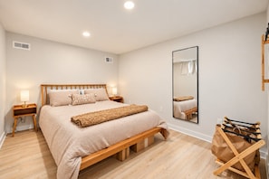 A bedroom with a wooden bed, bedside lamps, a large mirror, and a wooden bench. - Pet Friendly Home Near Vanderbilt & Centennial Park | 6-BR Home (Nashville)
