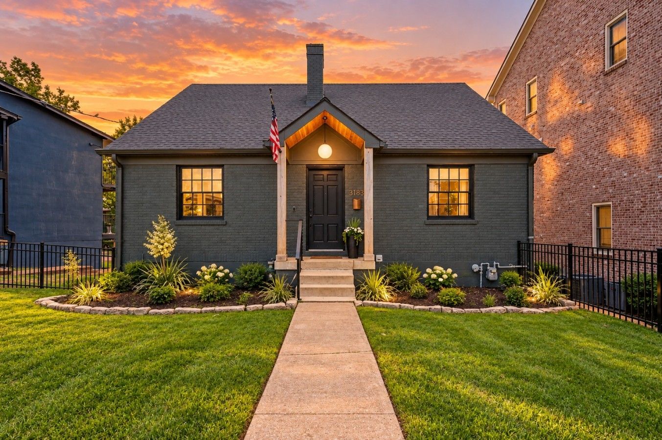 A two-story house with a dark grey exterior, a front porch, and a well-maintained lawn.