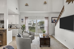 A spacious living area with a kitchen, a dining table, and a large window with curtains. - Driftwood Cove- Close to the beach (Galveston)