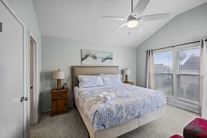 A bedroom with a bed, two bedside tables, a ceiling fan, a window with blinds, and a painting on the wall. - Driftwood Cove- Close to the beach (Galveston)