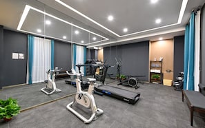 Un gimnasio moderno con diverso equipo de ejercicio, incluyendo cintas de correr y bicicletas estáticas, y un espejo grande en la pared.