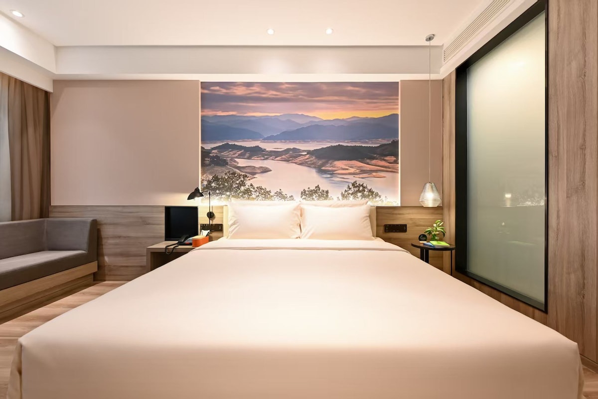 Una habitación de hotel moderna con una cama grande, un escritorio, una silla y vistas a un cuadro de paisaje.