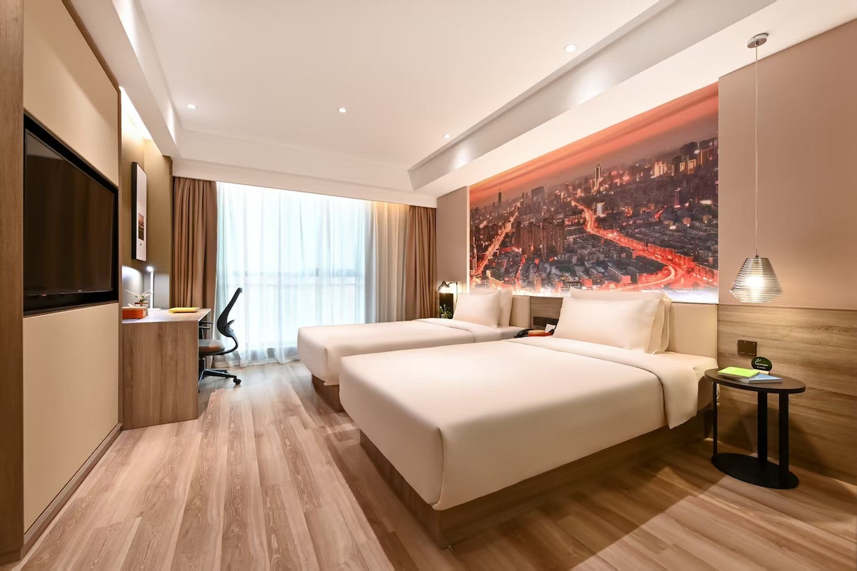 Habitación de hotel con dos camas, un escritorio, un televisor y vistas a la ciudad.