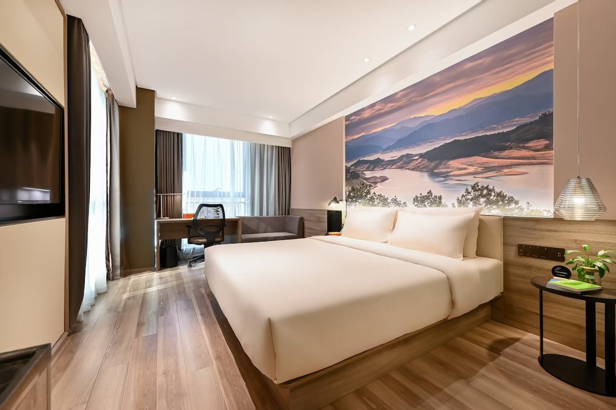 Habitación de hotel con una cama grande, un escritorio, una silla, un televisor y un cuadro de un paisaje.
