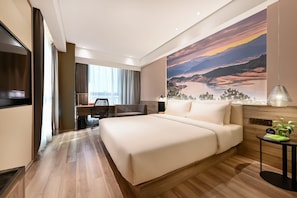 Habitación de hotel con una cama grande, un escritorio, una silla, un televisor y un cuadro de un paisaje.