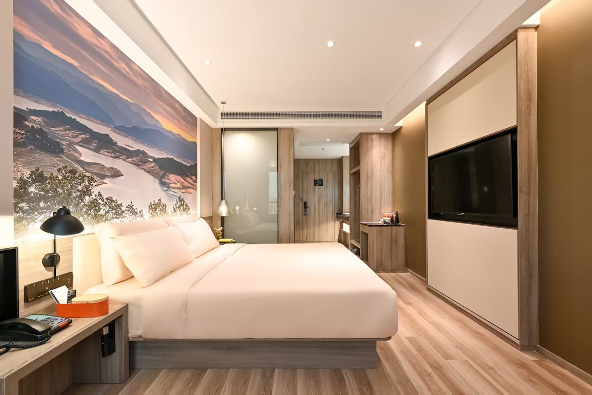 Habitación de hotel moderna con una cama grande, televisión, escritorio con lámpara y un mural panorámico en la pared.