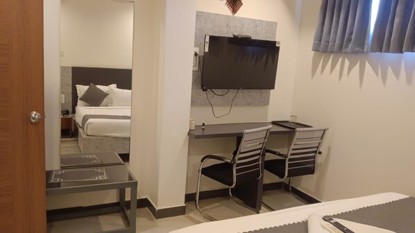 Habitación de hotel con cama, escritorio, dos sillas, televisor y una mesita.