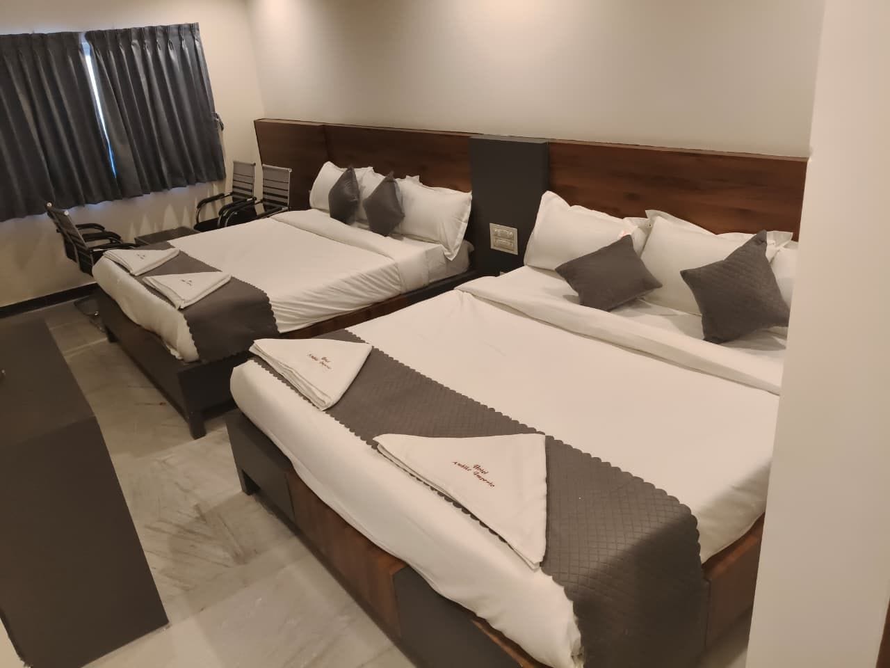 A hotel room with two beds, each with pillows and a blanket.