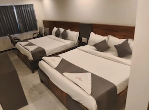 A hotel room with two beds, a wooden headboard, and a window with curtains. - Hotel Ambika Imperio (Vijayawada)