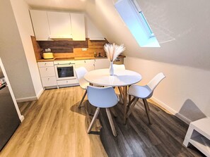 Eine kompakte Küche mit Essbereich, inklusive einem weißen Tisch und Stühlen, einem kleinen Backofen und einem Fenster über der Spüle.