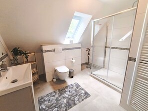Ein modernes Badezimmer mit Oberlicht, einer Duschkabine aus Glas und einem weißen Waschbecken.