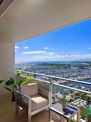 A balcony with a view of a marina, a cushioned chair, a small table, and a potted plant. - Stunning Wide Ocean View Home, with 2 Queen Beds (Honolulu)