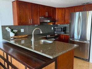 A kitchen with granite countertops, stainless steel appliances, wooden cabinets, and a built-in oven. - Stunning Wide Ocean View Home, with 2 Queen Beds (Honolulu)