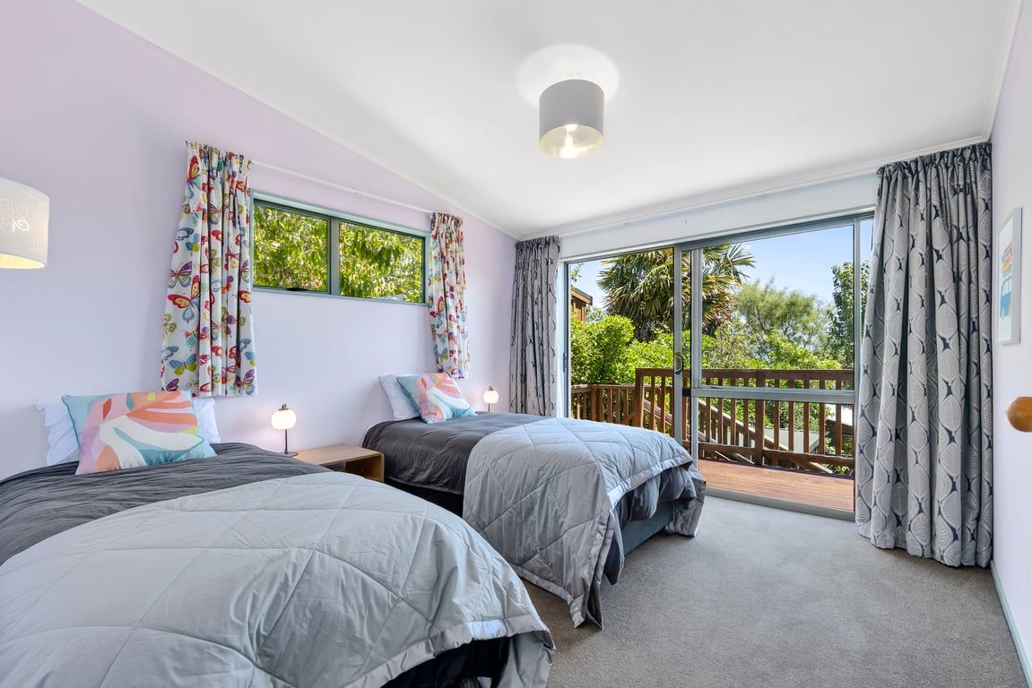A bedroom with two beds, a balcony, and a view of greenery.
