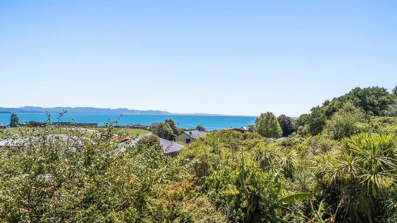 A coastal landscape with a view of the sea, vegetation, and buildings in the foreground.