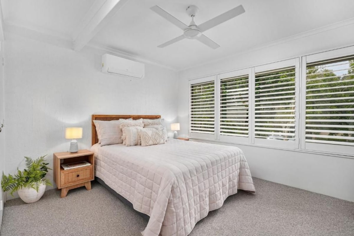 A bedroom with a bed, bedside tables, a ceiling fan, and a window with blinds.