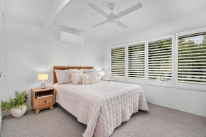 A bedroom with a bed, bedside tables, a ceiling fan, and a window with blinds. - Jindiburra Coastal Haven at Noosaville (Noosaville)