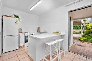 A modern kitchen with white cabinetry, a built-in oven, a sink, and a small island with stools. - Jindiburra Coastal Haven at Noosaville (Noosaville)