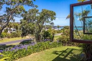 A lush garden with a variety of plants and flowers, a road, and a view of a body of water.