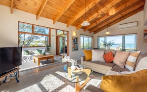 A spacious living room with a large TV, comfortable seating, and large windows offering a view of the outdoors.