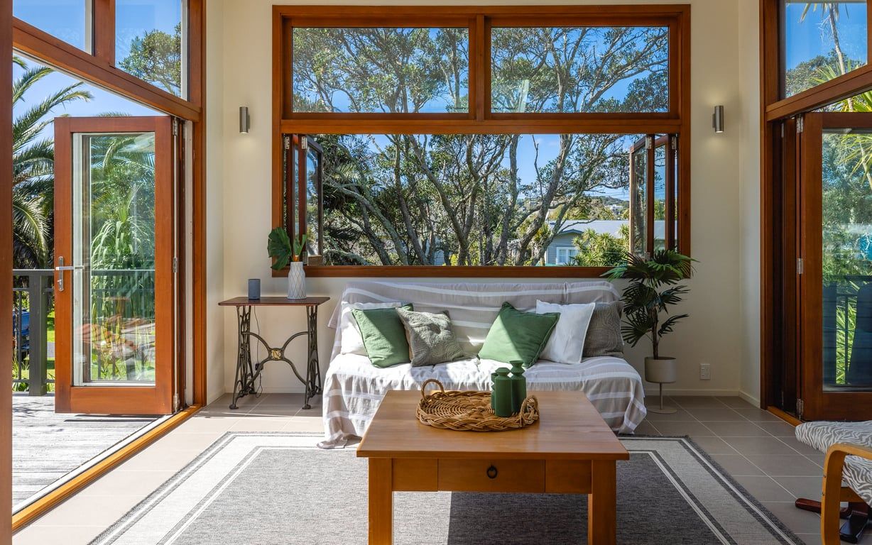 Una habitación con un ventanal grande, un sofá con cojines, una mesita y una planta en maceta.