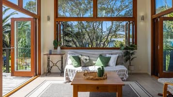 Una habitación con un ventanal grande, un sofá con cojines, una mesita y una planta en maceta.