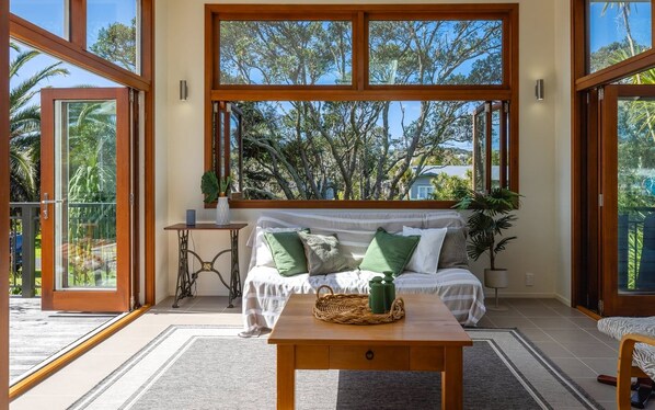 A room with a large window, a sofa with cushions, a small table, and a potted plant.