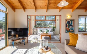A spacious living room with a large TV, wooden ceiling, and a view of the outdoors.