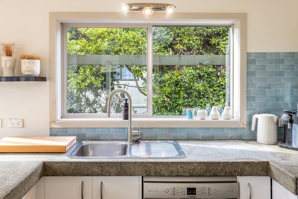 A kitchen with a window, stainless steel sink, Bosch dishwasher, and a coffee maker.