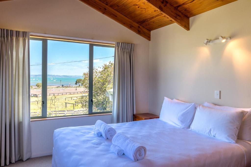 A bedroom with a large window, a bed with white linens, and a wooden ceiling.