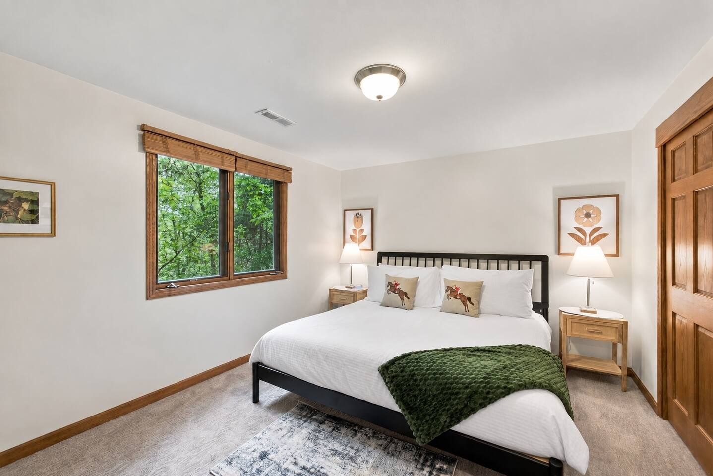 A bedroom with a large bed, a window with a view of trees, and two bedside tables with lamps.